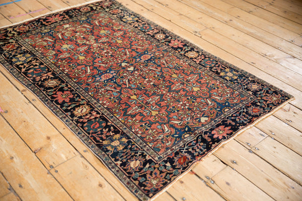Angled view of an antique Farahan Sarouk rug highlighting its madder red field and dark navy floral border.