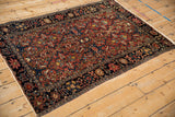 Detailed view of an antique Farahan Sarouk rug's madder red field and wide navy floral border.