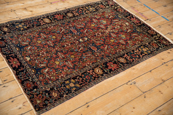 Angled view of an antique Farahan Sarouk rug with a madder red floral field and a dark navy border.