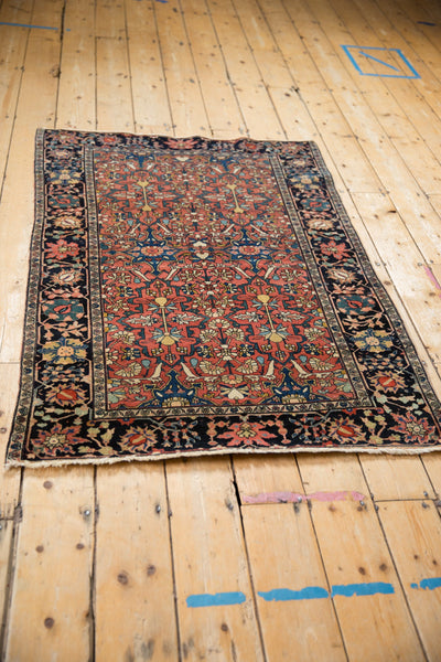 Full angled view of the antique Farahan Sarouk rug with a red floral field and navy border.