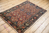 An antique Persian Farahan Sarouk rug shown from an angle, detailing its madder red floral field.