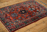 Angled view of a vintage Bijar rug highlighting its dense pile and navy-on-red floral medallion design.