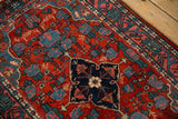 The navy shield medallion, cherry red field, and arabesque border of a vintage Persian Bijar rug.