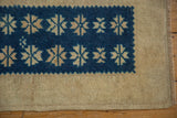 Distressed Oushak rug corner showing indigo geometric starbursts and wide beige border with even pile wear.