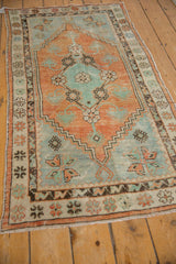 Angled view showing the distressed texture and floral medallion on a vintage terracotta and slate blue Oushak runner.