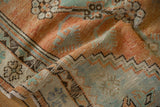 Folded corner of a distressed Oushak rug showing the worn pile and terracotta and mint motifs.