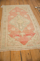 Angled view of a distressed Oushak rug with a soft pink field and a seafoam green medallion.