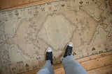Person's view looking down at a distressed Oushak runner's muted green medallion and low-pile texture.