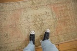 A person's view looking down at the worn, low-pile texture of a vintage Oushak rug.