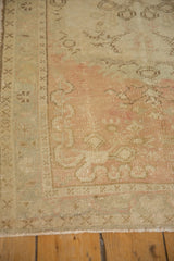 Corner of a distressed Oushak rug with faded dusty rose tones and an intact side cord selvage.