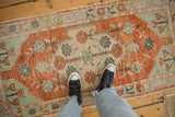 Distressed vintage Oushak runner with faded colors, viewed underfoot to illustrate scale.