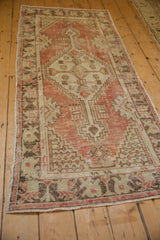 Angled view of distressed vintage Oushak runner with geometric pattern, red blush, ivory tones.