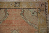 Corner detail of a distressed Oushak rug showing the worn pile, gold border, and short ivory fringe.