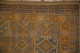 Distressed Anatolian rug corner, showing checkered and floral borders with subtle blue, gold, bronze hues.