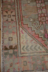 Distressed corner of a vintage Oushak rug with faded aubergine, silver, and magenta geometric patterns.