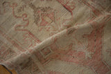 Folded section of the distressed Oushak rug with blush red motifs and worn pile.