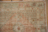 Worn, low-pile texture of a distressed Oushak rug in pale rust and seafoam with visible fringe.