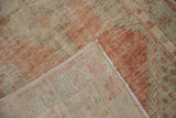A folded corner on the distressed Oushak rug reveals its hand-knotted foundation and worn pile.