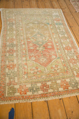 Angled view of a distressed Oushak rug's corner with geometric borders in sage, ivory, and orange.
