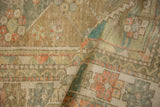 A corner of a distressed Oushak rug folded to show its low, time-softened pile and visible knots.