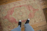 Distressed vintage Oushak rug showing its low pile texture in faded magenta and ivory tones.