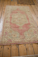A full-length angled view of a distressed vintage Oushak rug with a faded magenta and ivory palette.
