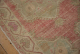 Worn, low pile on a distressed Oushak rug corner showing faded magenta and muted silver tones.