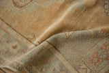 A soft fold reveals the low, evenly worn pile of a vintage Oushak rug in sand tones.