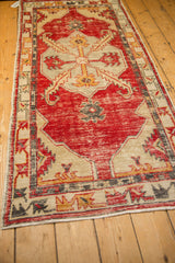 Angled view of a vintage Oushak runner showing its distressed red medallion and beige ground.