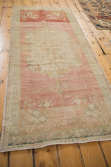 Distressed Oushak runner viewed at an angle, showing its abrashed pink field and seafoam border.