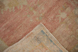 Folded corner of a distressed Oushak rug reveals the soft pink pile and hand-knotted weave.