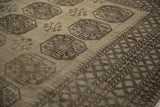 Distressed vintage Ersari carpet showing geometric gul motifs and distinct diamond borders in beige and brown.