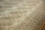 Distressed Ersari carpet showing ivory gul medallions and geometric patterns with soft green-blue tones.