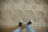 Distressed Ersari carpet showcasing ivory and dusty teal geometric medallions and worn texture.