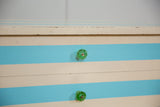 Faceted green glass knobs on the aqua and ivory striped drawers of a vintage nightstand.