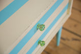 Angled view of the faceted green glass knobs on the ivory and aqua striped nightstand.