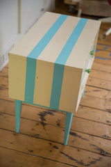 Angled view of the ivory and aqua striped nightstand, showing its green drawer knobs.