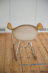 Back profile of the Eames rocking chair with its beige molded shell and chrome wire base.
