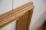 Carved foliate pattern and golden finish on a vintage wood picture frame corner.