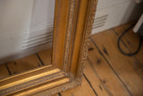Vintage golden wood picture frame corner, showing carved leaf motifs and textured finish.