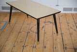 Mid century coffee table's textured beige top, dark edge, and tapered black leg.