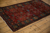 Vintage Persian Hamadan rug from an angle, showcasing its rich ruby red field and dense Herati pattern.