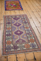 Distressed Oushak rug corner; aubergine field, ivory border with terracotta and purple geometric blossoms.