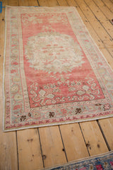 Angled view of a distressed Oushak rug showing its ivory medallion on a blush pink field.