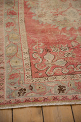 Angled corner view of a distressed Oushak rug showing the floral border and evenly worn pile.