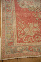 Angled view of the vintage Oushak's border showing floral patterns in blush pink and silver tones.