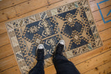 Distressed Oushak rug with geometric hook and latch patterns; dark denim blue, ivory, beige.