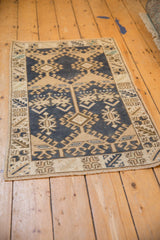 Distressed Oushak rug corner showing dark denim blue, beige geometric patterns, and woven selvage.
