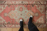 A person standing on a vintage Oushak runner, showing its scale and distressed dusty blush pattern.