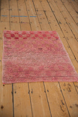 Angled view of a distressed Turkish Tulu rug with a shaggy pile in shades of dusty rose and raspberry.